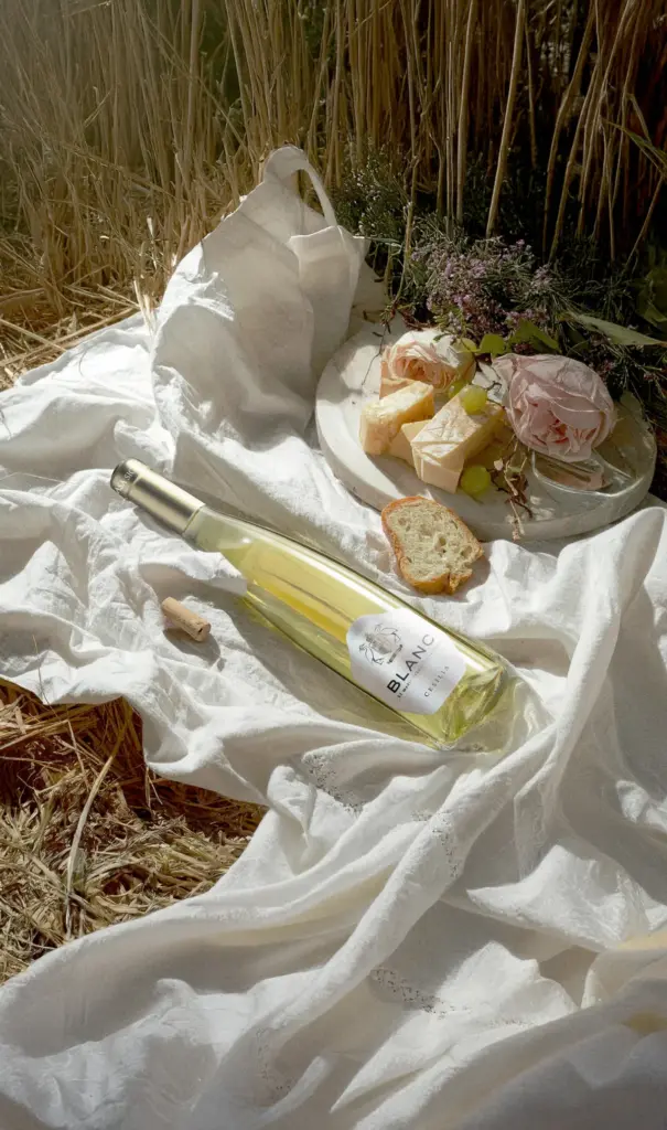 Botella de Cesilia Blanc con quesos y flores sobre un mantel de lino